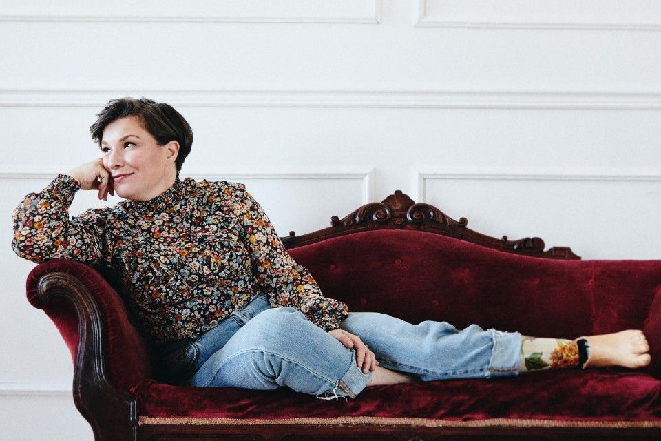 Christa Couture, a left leg amputee, sits pensively on a red velvet couch with hand on chin