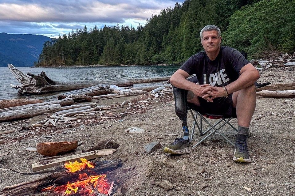 Erez Avramov a right leg below-knee amputee sitting on log near beach campfire